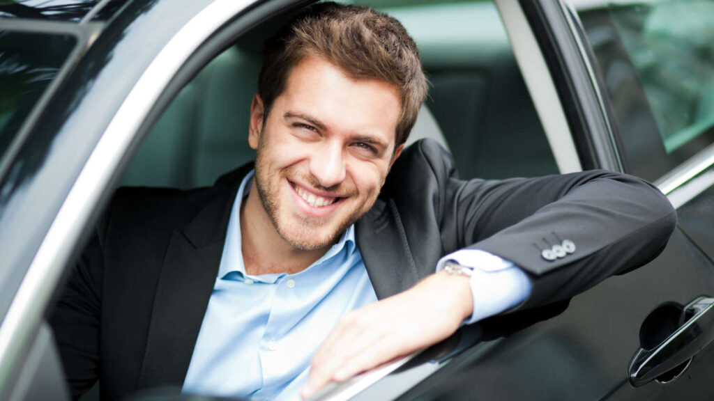 Uśmiechnięty mężczyzna siedzi w samochodzie, który jest rzeczowym aktywem trwałym w jego firmie w Holandii, czyli materiële vaste activa.